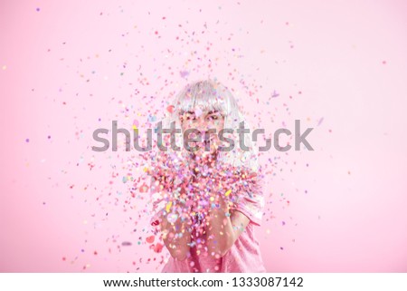 Funny Girl with silver hair gives a smile and emotion on pink background. Young woman or teen girl with confetti. Concept of holiday and party.