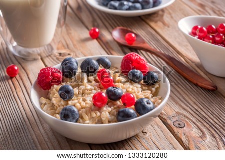 Close up view of porridge with blueberries and raspberries and grain bread on wooden background. Royalty-Free Stock Photo #1333120280