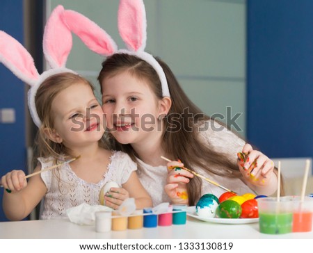 Beautiful little girls sisters, has happy fun smiling face, pretty eyes, white t-shirt, hare ears, paint easter eggs. Child portrait and kids hobby concept. Holiday accessories. 