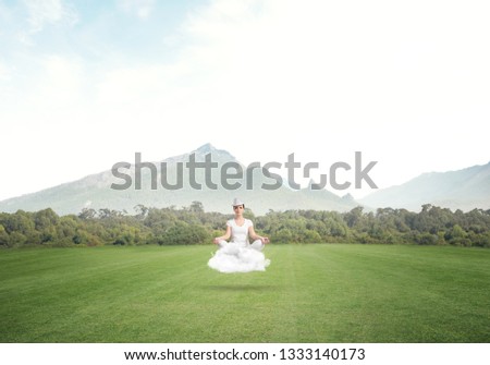 Young woman keeping eyes closed and looking concentrated while meditating on cloud in the air with beautiful and breathtaking landscape on background.