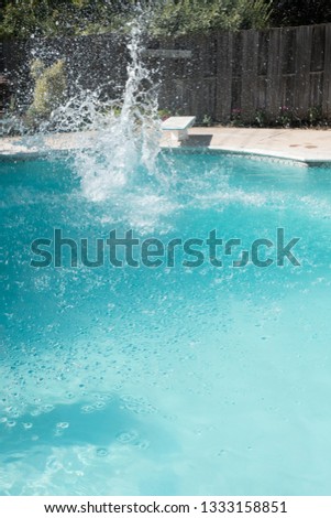 Guy jumps into an outdoor swimming pool in the summer. Man lands in pool from jumping off diving board doing cannon ball into a pool with big splash as he lands in the deep end of the pool. Royalty-Free Stock Photo #1333158851