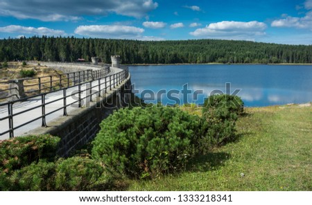 Water surface of dam "Bedrichov" in "Jizera" mountains. The sky with clouds are mirroring in the water surface. Summer day in the nature with green vegetation. Royalty-Free Stock Photo #1333218341