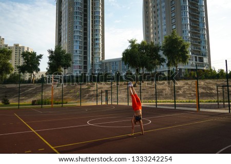Theme sport and a healthy lifestyle. Wide angle Caucasian woman with tattoo training outdoors in summer at a sports stadium. Exercise walking on the hands. Sports girl handstand.