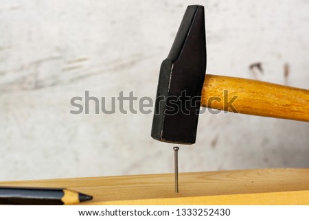 Male hand in a black construction glove hammering a nail with a hammer against the background of a concrete wall