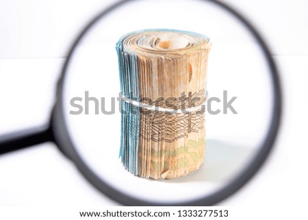Focus on a thick roll of upright banknotes without visible value mark seen through a magnifying glass. Clean studio shot of currency with magnify tool against a white background.