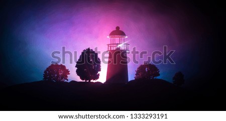 Artwork decoration. Lighthouse with light beam at night with fog. Old lighthouse standing on mountain. Table decoration. Toned background. Moonlighting. Selective focus