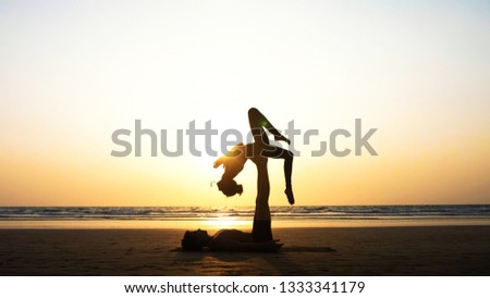 Silhouette of fit sporty couple practicing acrobatic yoga with partner together on the beach in slow motion. Female acrobat balancing on feet of her partner in fylfot shape