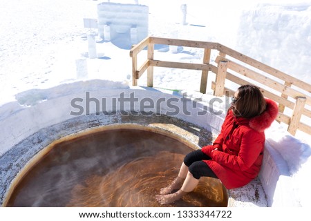 Asian young beauty woman relaxing in hot springs and enjoy the beautiful mountain view with snow in winter.Japanese natural mineral water Onsen at Ice Igloo Village in Lake Shikaribetsu,Hokkaido,Japan
