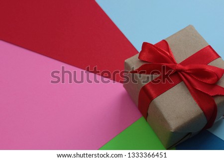 box with a red bow stands on paper of different colors