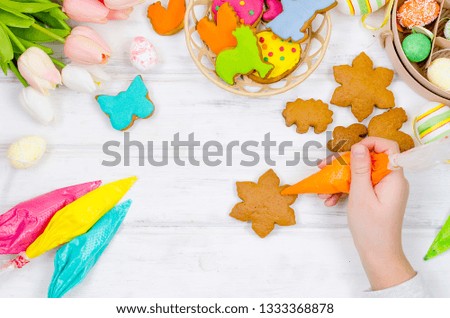 Child hands decorating honemade gingerbread with icing sugar using a pipping bag. Easter Treats. Handmade cookies, standing on the table. series of step by step photos. Royalty-Free Stock Photo #1333368878