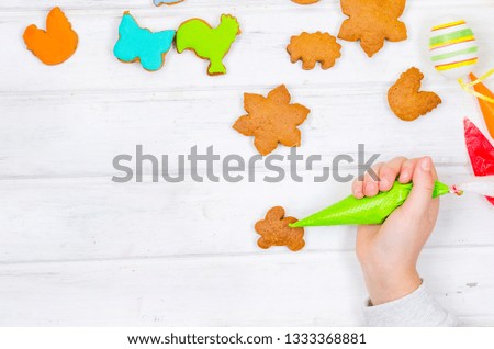 Child hands decorating honemade gingerbread with icing sugar using a pipping bag. Easter Treats. Handmade cookies, standing on the table. series of step by step photos. Royalty-Free Stock Photo #1333368881