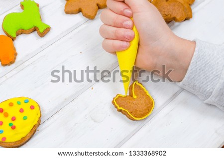 Child hands decorating honemade gingerbread with icing sugar using a pipping bag. Easter Treats. Handmade cookies, standing on the table. series of step by step photos. Royalty-Free Stock Photo #1333368902