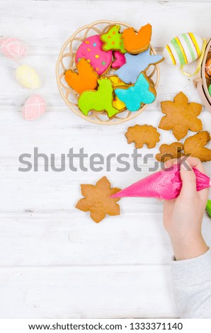 Child hands decorating honemade gingerbread with icing sugar using a pipping bag. Easter Treats. Handmade cookies, standing on the table. series of step by step photos. Royalty-Free Stock Photo #1333371140