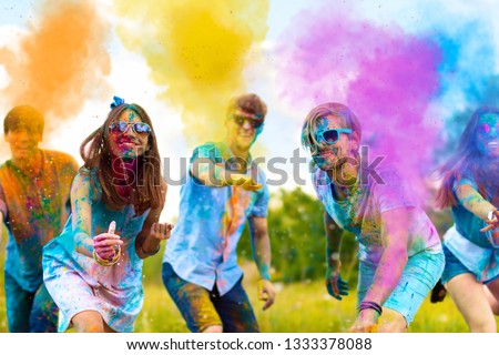 Cheerful and happy soiled friends throw bright paints on camera and smiling. Company of young people in sunglasses having fun with holi paints on spring summer festival. Holi party concept. Royalty-Free Stock Photo #1333378088