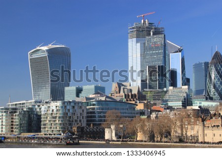 Modern buildings of the City of London taken from the River Thames in London, England, contrasting with the historic Tower of London in the foreground on a clear, sunny day