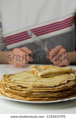 Person eating Pancakes on the white plate by knife and fork . Many pancakes are stacked. Thin pancakes with crispy crust. Food background.