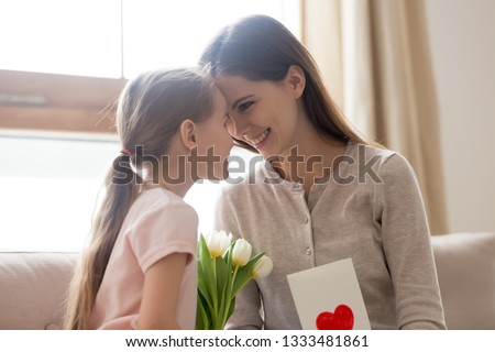 Happy mom and little kid daughter bonding celebrating mothers day, cute child girl making surprise congratulating mom with birthday holding spring flowers and greeting card, family love celebration