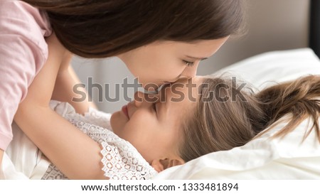 Loving mother gently kissing cute kid daughter wishing good night sweet dreams or waking up early, caring mom embracing little child girl lying in bed awaking enjoying happy family warm morning