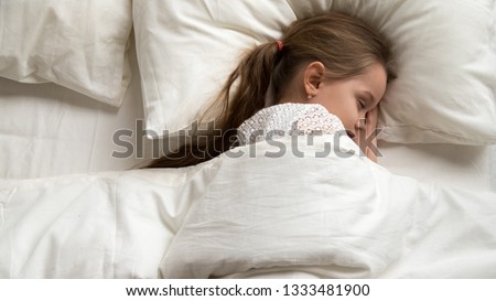 Adorable cute little baby girl sleeping alone in comfortable bed lying on soft pillow covered with warm duvet, calm kid resting asleep in good night healthy peaceful sleep nap in bedroom, top view