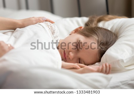 Loving mom hands touching sleeping cute small daughter waking up little child lying asleep in bed covered with duvet in family good morning, caring parent mother stroking kid fall asleep in bedroom