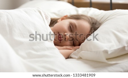 Calm kid girl sleeping well alone on soft pillow covered with warm blanket duvet lying in comfortable bed, cute little child resting asleep on white sheet napping in good night healthy peaceful sleep