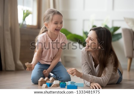 Happy family mom baby sitter and little kid daughter laughing playing with wooden blocks sit of warm floor, joyful mother having fun with child girl enjoy funny activity laughter at home together Royalty-Free Stock Photo #1333481975