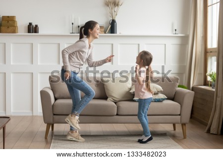 Happy young mom baby sitter sister and cute funny little kid daughter laughing dancing in living room together, cheerful active mother with child girl having fun enjoy moving to music playing at home