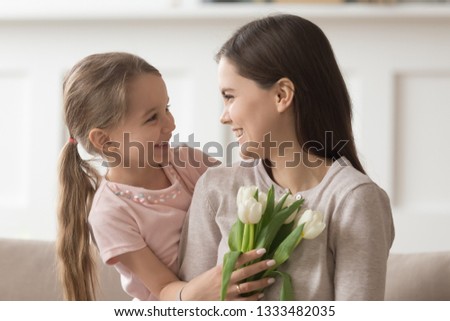 Happy grateful mom holding spring flowers on 8 march or mothers day gift from cute kid smiling looking at little daughter presenting tulips to young mum at home showing family care love to mommy