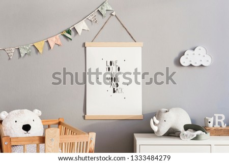 Stylish and cute scandinavian decor of newborn baby room with mock up poster, natural toys, hanging decor flags and cloud, wooden cradle, plush rhino  and teddy bears. Grey walls.