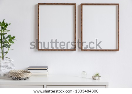 Stylish white home decor of interior with two brown wooden mock up photo frames with books, beautiful plant in stylish pot, air plants and home accessories. Minimalistic scandinavian room.