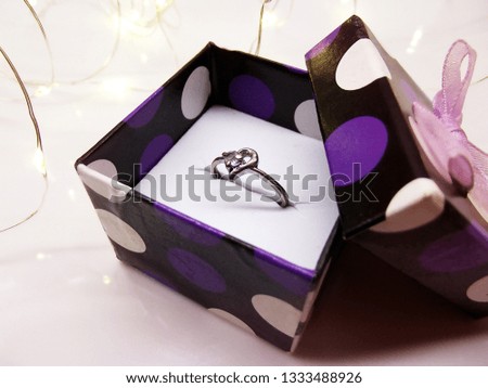 It is a close up picture of a ring in the gift box. The background is white with micro led light garland.