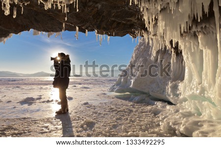 A tourist in the winter on Lake Baikal takes pictures of an ice grotto, and the sun shines and makes its way between the face and the camera. Unusual solar pictures from travel