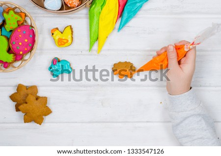 Child hands decorating honemade gingerbread with icing sugar using a pipping bag. Easter Treats. Handmade cookies, standing on the table. series of step by step photos. Royalty-Free Stock Photo #1333547126