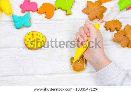 Child hands decorating honemade gingerbread with icing sugar using a pipping bag. Easter Treats. Handmade cookies, standing on the table. series of step by step photos. Royalty-Free Stock Photo #1333547129