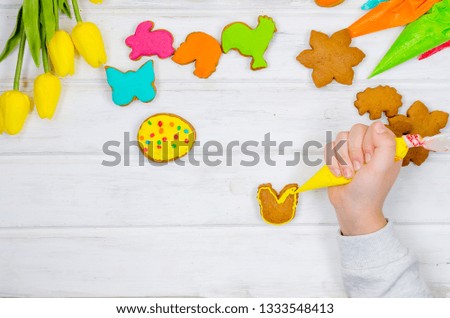 Child hands decorating honemade gingerbread with icing sugar using a pipping bag. Easter Treats. Handmade cookies, standing on the table. series of step by step photos. Royalty-Free Stock Photo #1333548413
