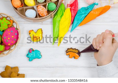 Child hands decorating honemade gingerbread with icing sugar using a pipping bag. Easter Treats. Handmade cookies, standing on the table. series of step by step photos. Royalty-Free Stock Photo #1333548416