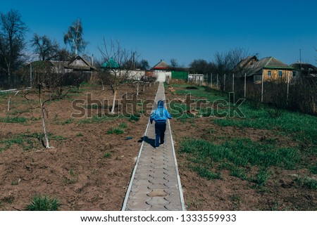 a small child runs along the road in the village, around young trees and un-excavated land, virgin soil. spring plant growth on the farm. village