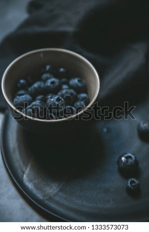 dark food photography of stone ware bowl with blueberries in rembrandt lighting coming from one window with slate plate and dark linen
