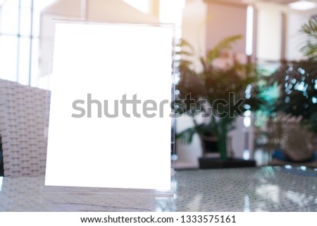 Mock up white Label on the table for blank menu frame in restaurant for booklets with sheets paper, Stand for acrylic tent card Used for Menu Bar, blur of green background insert for text of customer.