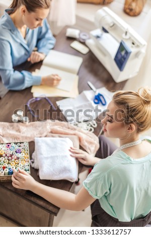 2 young beautiful female dressmakers cooperating in their own studio working as a team on new order. Small Business, partnership and friendship concept