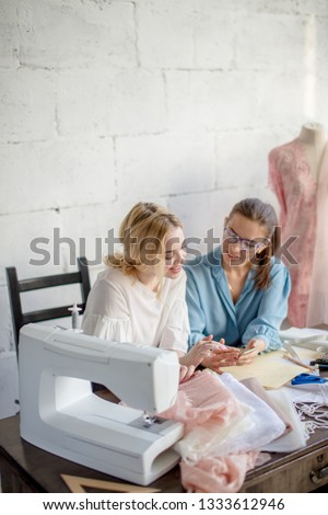 Female dressmaker showing design to her client, sitting together at tailoring workshop.
