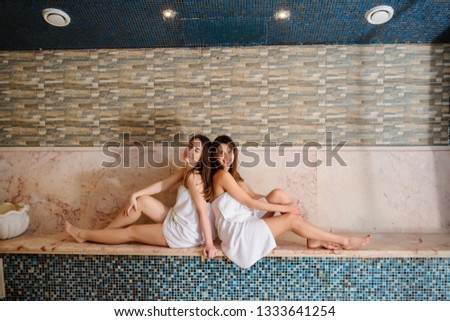 close up photo of two beautiful women wearing white towels relaxing in hamam