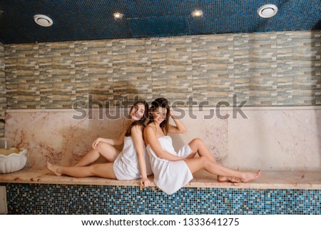 close up photo of two beautiful women wearing white towels relaxing in hamam