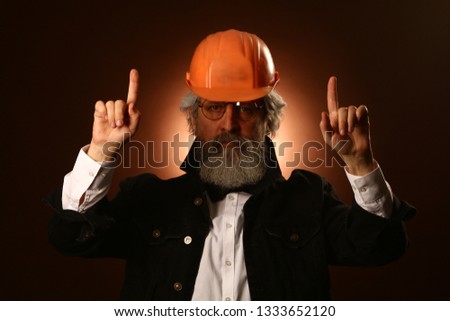 an elderly worker in a helmet gestures warning signs, close-up studio portrait