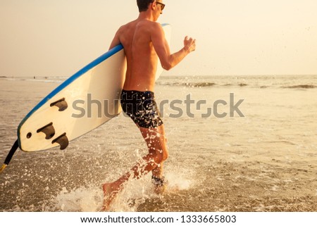 A surfer man with his surfboard going to meet the sea waves evening sunset on the beach.male freelancer surfing on vacation in a tropical country paradise island