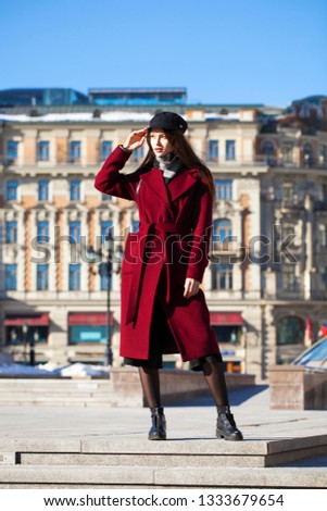Full body portrait. Young beautiful brunette woman in stylish in a long burgundy coat walking in spring street