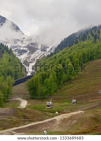 Cable car on the spring slope with melted snow. Snowy mountains in the fog. Krasnaya Polyana, Sochi, Russia