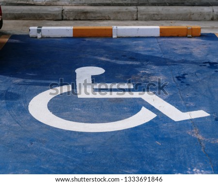 Handicap symbol on road, traffic and pedestrians in background. Parking for disabled people in gas station