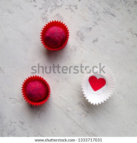 Two red truffles with raspberry filling in red candy wrappers and one white wrapper with a red heart inside on a light grey background. Love concept. 
