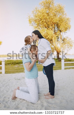 Young and beautiful pregnant brunette in a white shirt on a beach with her husband and little son